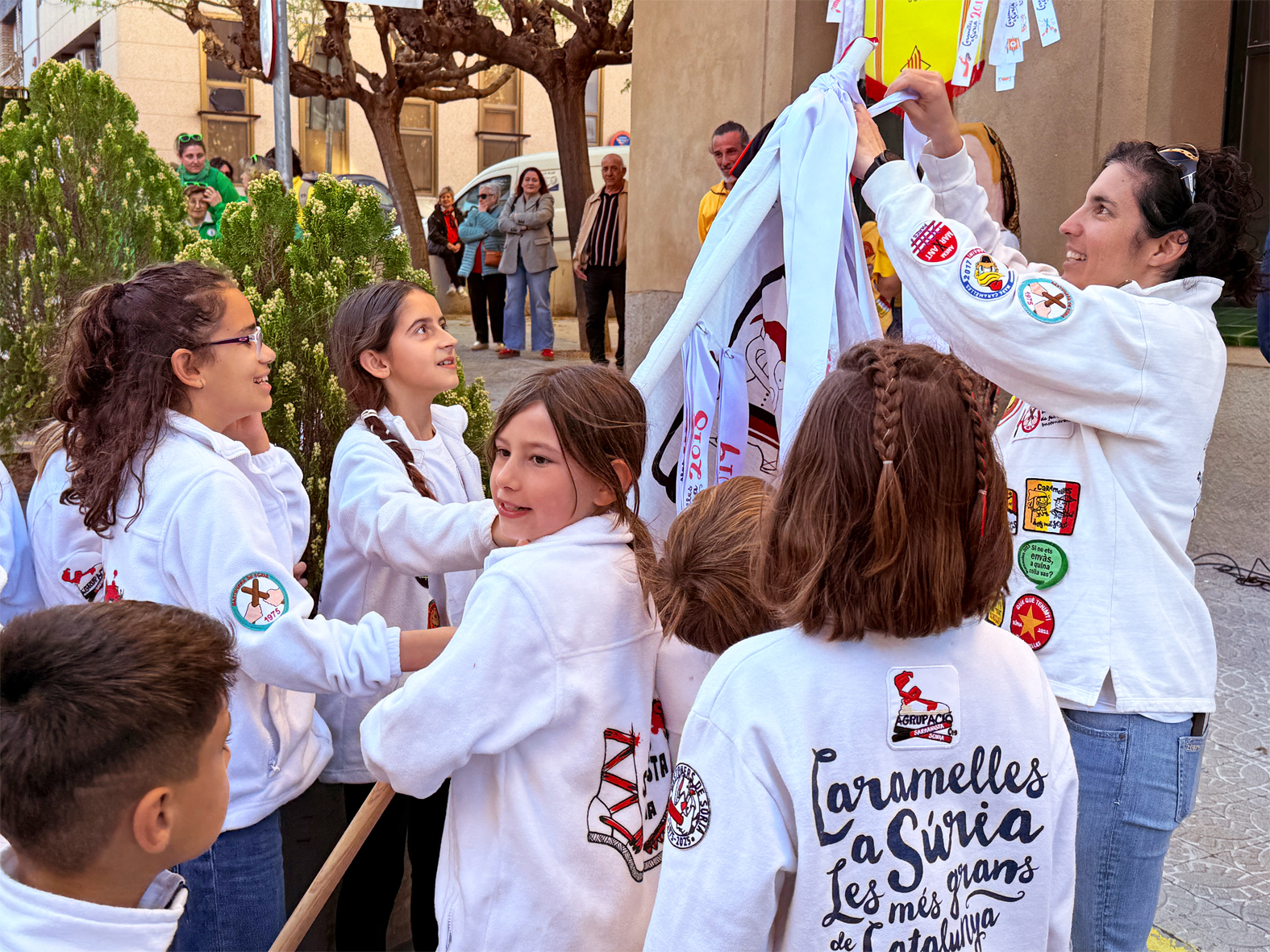 La regidora de Festes, Alba Martínez, lliura la cinta commemorativa a la colla Infantil de l'Agrupació Sardanista en l'acte d'inici de les Caramelles de Súria, al davant de la Casa de la Vila.