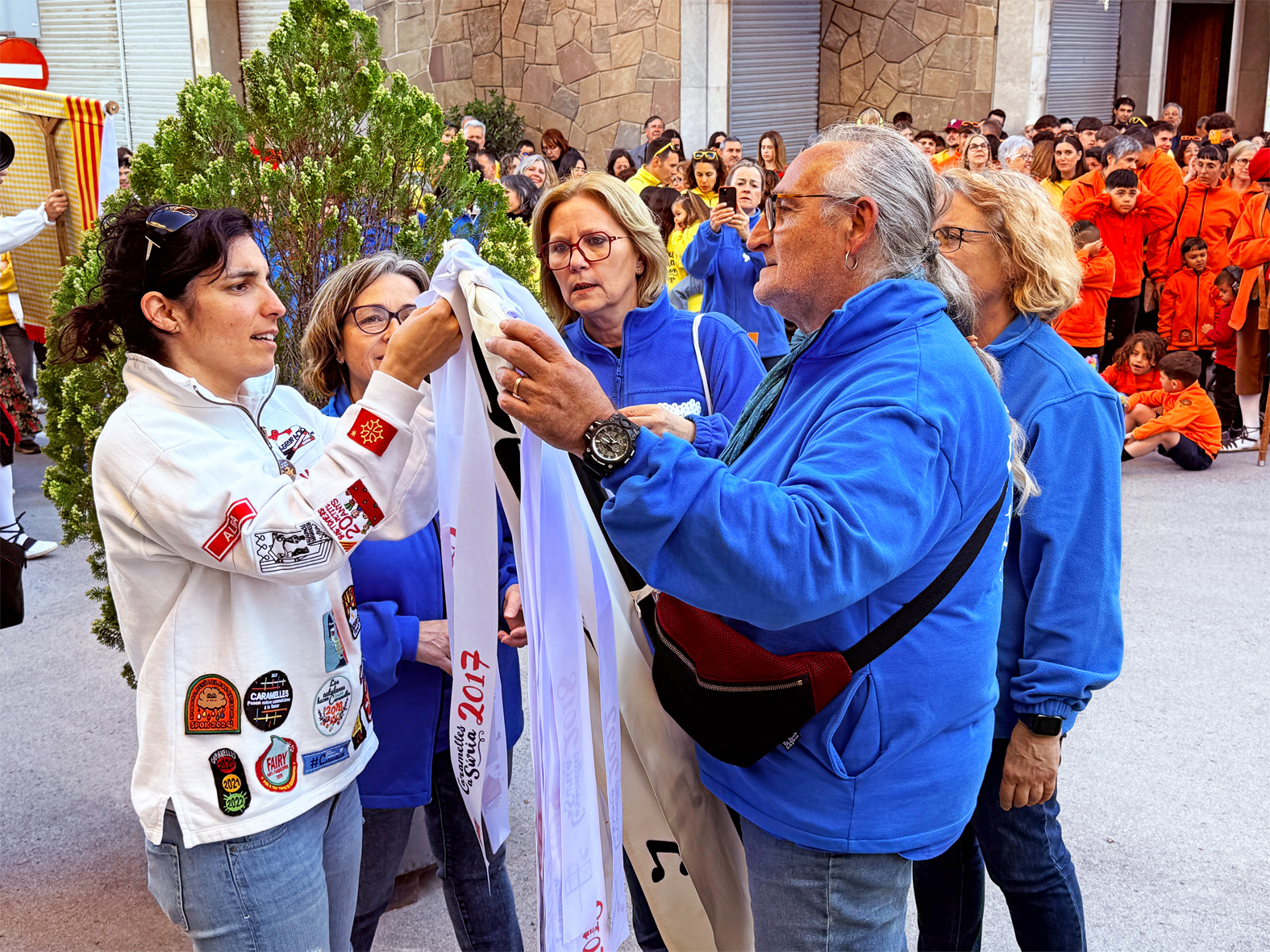 La regidora de Festes, Alba Martínez, lliura la cinta commemorativa a la colla de la Coral Sòrissons en l'acte d'inici de les Caramelles de Súria, al davant de la Casa de la Vila.
