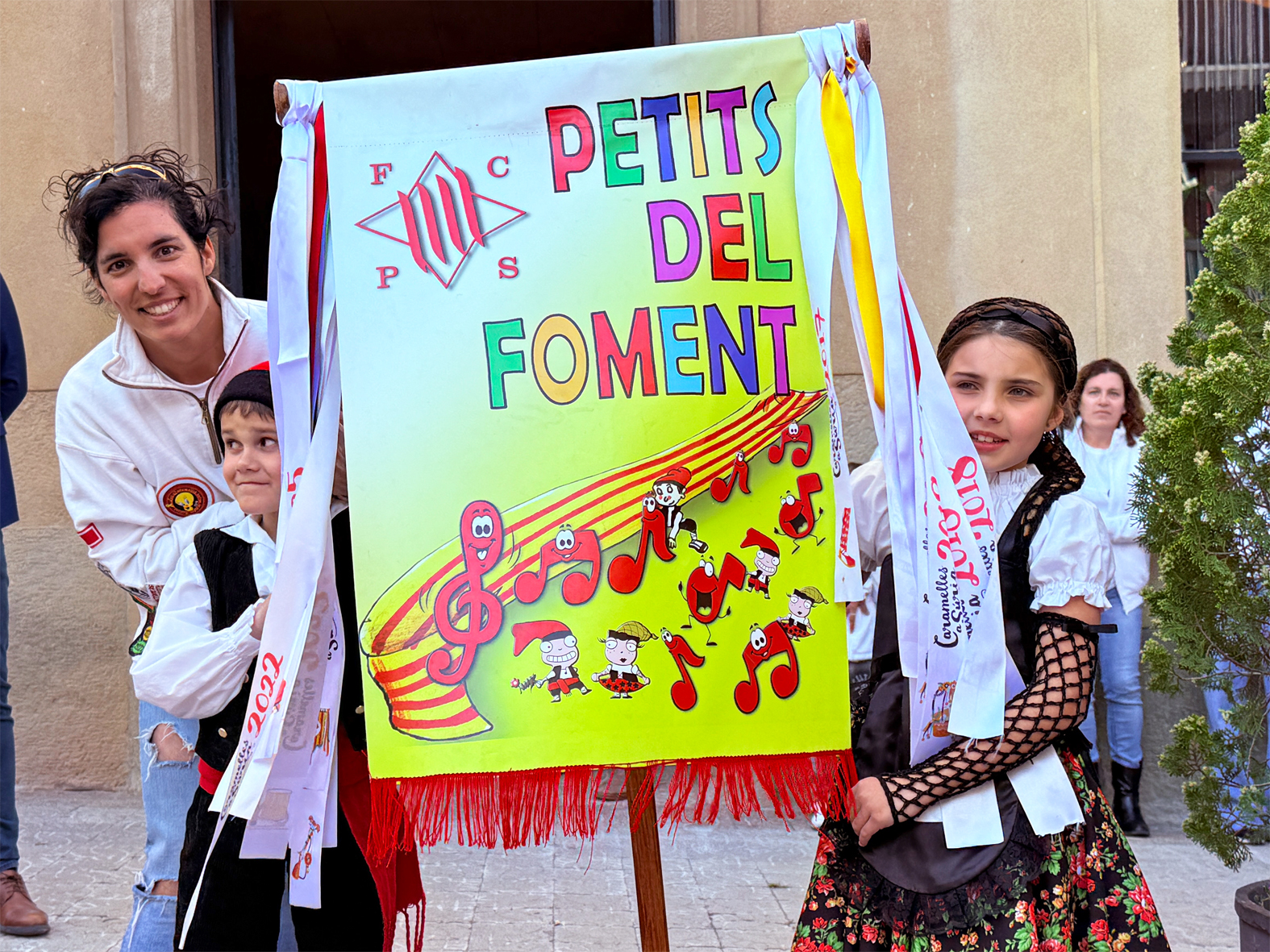 La regidora de Festes, Alba Martínez, lliura la cinta commemorativa a la colla Infantil del Foment Cultural, en l'acte d'inici de les Caramelles de Súria, al davant de la Casa de la Vila.