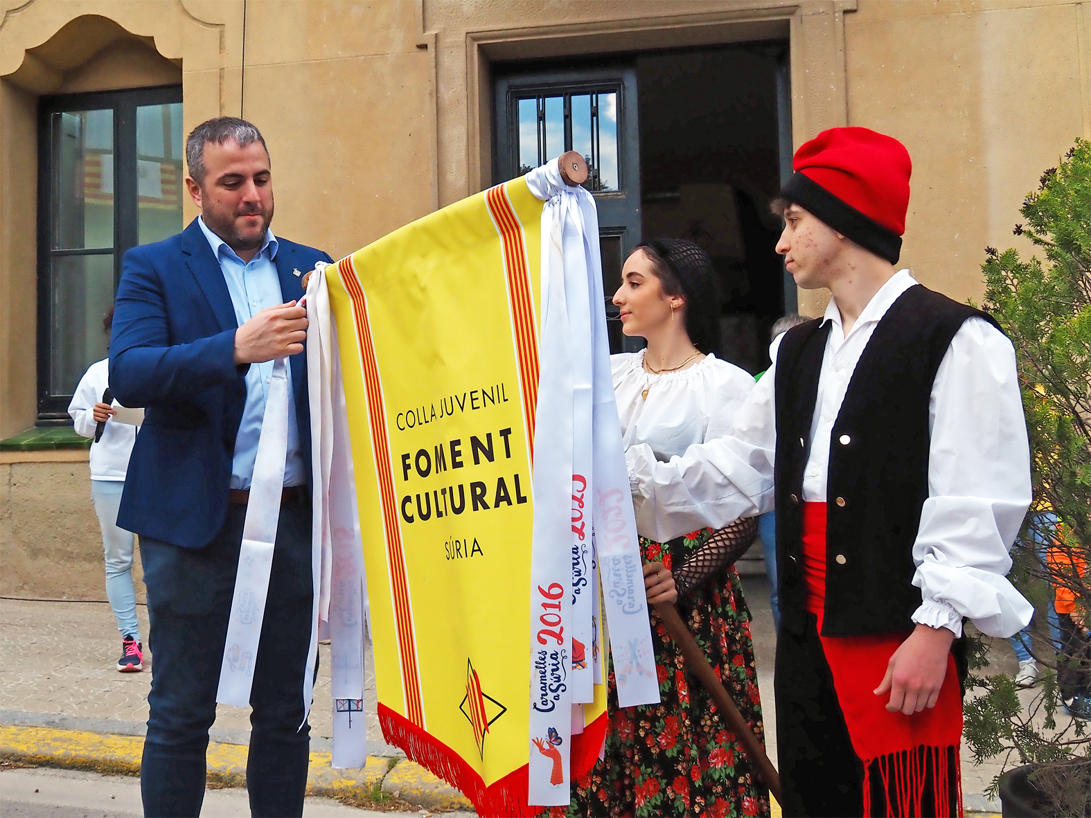 L'alcalde Albert Cober&oacute; lliura la cinta commemorativa a la colla Juvenil del Foment Cultural en l'acte d'inici de les Caramelles de S&uacute;ria, al davant de la Casa de la Vila.